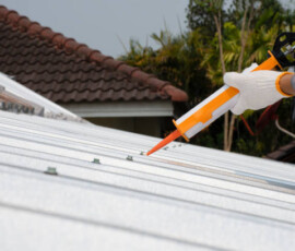 Worker man hand using glue gun with silicone adhesive or manual caulking gun with polyurethane to fix the metal steel on the roof. Installing and building construction concept.
